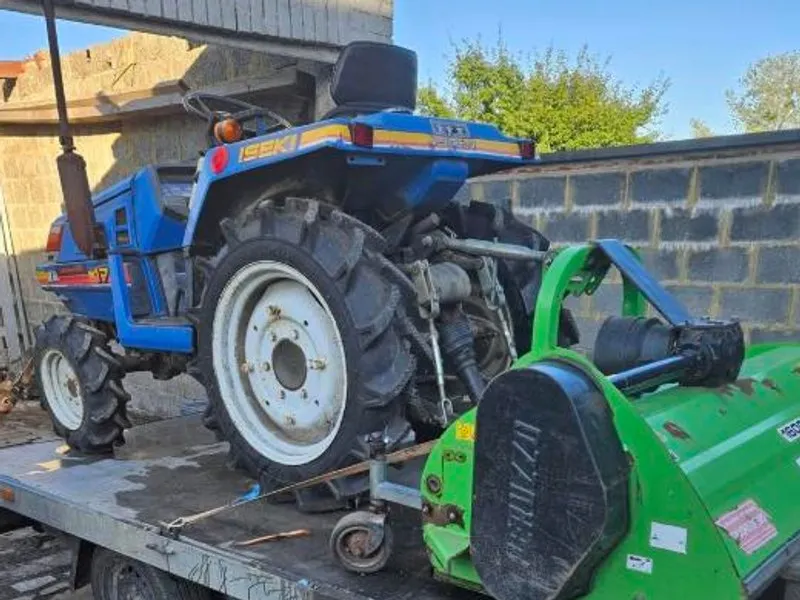 Micro-tracteur Iseki bleu attelé à un gyrobroyeur, sur remorque plateau