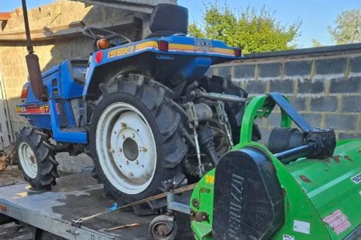 Micro-tracteur Iseki bleu attelé à un gyrobroyeur, sur remorque plateau